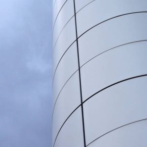 curved grey metallic architectural cladding on a modern industrial building against a blue cloudy sky